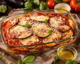 Un plat de parmigiana di melanzane, gratiné et garni de parmesan râpé, prêt à être dégusté. Des aubergines fraîches et des tomates entourent ce délice italien.