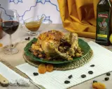 Pollo asado relleno, dorado y jugoso, servido en plato verde con pasas y orejones. Acompañado de vino tinto y aceite de oliva.