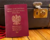Polski paszport i brązowa walizka na drewnianym tle.