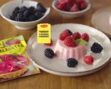 Panna cotta z malinami i jeżynami, obok opakowanie galaretki malinowej.