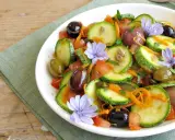 Insalata di zucchine fresca con pomodori, olive, carote e fiori di cicoria, un piatto colorato e leggero.