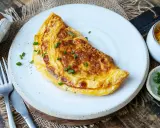 Goldbraunes Omelett mit Käse und Schnittlauch, perfekt für ein schnelles Omelette Rezept. Daneben: Eier, geriebener Käse und frischer Schnittlauch.