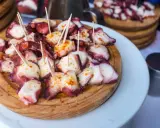 Pulpo a la gallega servido en tabla de madera, con palillos y espolvoreado con pimentón.