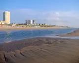 Piękny dzień nad morzem w Holandii. Piaszczysta plaża, spokojna woda i nowoczesne budynki w tle tworzą malowniczy krajobraz.