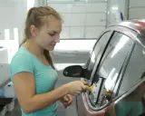 Kobieta przyciemnia szyby w samochodzie, używając rakli. Samodzielne przyciemnianie szyb wymaga precyzji.