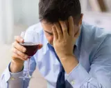 Hombre con copa de vino tinto, con la mano en la frente, buscando alivio en un vino sin histamina.