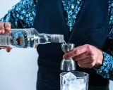 Barman nalewa Żubrówkę do jiggera, przygotowując drinka. W tle szklanka z lodem. Wataha wodka w butelce.