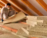 Trabajador instala aislamiento en ático, buscando un bajo coeficiente k para optimizar la eficiencia energética.