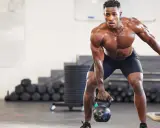 Ein Mann mit starkem Muskelaufbau hebt eine Kettlebell. Seine Anstrengung spiegelt die Ergebnisse von intensiven Trainingseinheiten wider, wie sie in Studien zum Muskelaufbau untersucht werden.