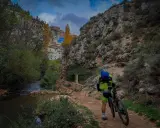 Ciclista en la ruta de las esculturas Bogarra, junto a un río y un pueblo en la ladera.