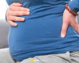 Ciężarna kobieta trzyma się za brzuch i plecy, odczuwając dyskomfort. To może być objaw biegunki przed porodem.