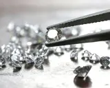 Un diamante etico, scintillante, tenuto da una pinzetta, circondato da altri brillanti su una superficie metallica.