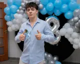 Chłopak w błękitnej koszuli z rozetką "18th Birthday" i balonami.
