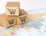 Trzy kartony z ikonami koszyków na zakupy na mapie świata. Symbolizują handel transgraniczny i globalny e-commerce.