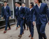 A group of men in navy suits walk down a sidewalk. They are all wearing brown dress shoes, proving you can wear brown shoes with a navy suit.
