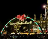 Wiedeński jarmark świąteczny w blasku świateł. Tłumy ludzi spacerują pod łukiem z napisem "Wiener Christkindlmarkt", w tle widać zabytkowe budynki i choinkę.