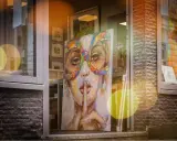 A vibrant painting of a woman in a colorful mask hints why rich people buy art: for beauty, status, and a touch of mystery.