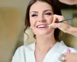 Maquillaje para madrina de boda: una mujer sonríe mientras le aplican brillo labial.