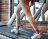 Frau trainiert auf Laufband, 12-3-30 Methode. Beine in Leggings und weißen Sneakern bewegen sich im Rhythmus.