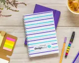 Pomysł na kalendarz: kolorowy notatnik z napisem "design your life", obok długopisy, karteczki i kawa.