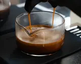 Frisch gebrühter Espresso fließt in ein Glasgefäß, die goldbraune crema de cafe bildet eine samtige Schicht.