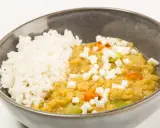 Un tazón de arroz blanco junto a un guiso cremoso de lentejas rojas con trozos de queso y verduras.