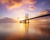 Ponte sospeso sull'acqua calma, con un cielo colorato da un tramonto mozzafiato. Una foto da fare al tramonto, perfetta per catturare la magia del momento.