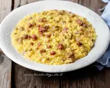 Un cremoso risotto con salsiccia, servito in un piatto bianco su un tavolo di legno rustico.