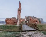 Ruiny zamku w województwie łódzkim, z drewnianym mostkiem prowadzącym do ceglanych murów.