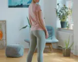 Frau in Sportkleidung, bereit für ein Workout. BWS mobilisieren für mehr Flexibilität. Bücherregal und Pflanzen im Hintergrund.