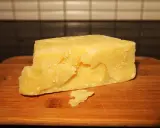 Kawałek żółtego sera typu Grana na drewnianej desce.