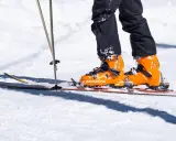 Pomarańczowe buty narciarskie Scarpa na nartach, z kijkami narciarskimi w śniegu.
