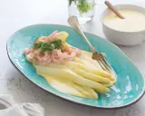 Białe szparagi z krewetkami i sosem holenderskim na turkusowym talerzu.