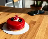 Un délicieux entremet fruit rouge, glacé et garni de framboises fraîches, attend sur une table en bois.