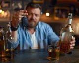 Mężczyzna trzyma kluczyki do samochodu, zastanawiając się, czy jestem pijany. Obok butelki i szklanka alkoholu.