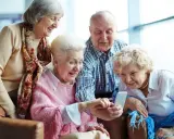 Cztery starsze osoby śmieją się, patrząc na telefon. Może sprawdzają, jak sprawdzić nfz kolejka do sanatorium?