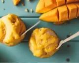 Jak zrobić sorbet? Dwa pucharki z mango sorbetem i kawałki świeżego mango na turkusowym tle.