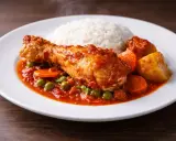 Estofado de pollo con arroz blanco, zanahorias y guisantes en una salsa roja.