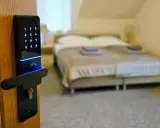 Cyfrowa klamka z klawiaturą numeryczną i niebieskim podświetleniem, symbolizująca digitalizację w hotelarstwie. W tle łóżko.