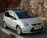 Biały Ford S-Max 2.0 TDCI pokonuje zakręt na malowniczej drodze wśród jesiennych drzew i skał.