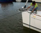 Un homme en gilet de sauvetage ajuste la pendille du bateau, une corde verte s'étendant sur l'eau calme.