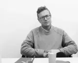 Shane Schneck, en man med glasögon, sitter vid ett bord med en ljus tröja och en skjorta.