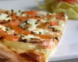 Tranche de flammekueche saumon, oignons et fromage, avec une salade verte en arrière-plan.