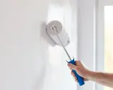 Mano con rodillo pintando una pared blanca, renovando el hogar.