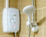 Ein weißer Boiler für die Dusche mit Reglern und eine Duschbrause an der Wand.