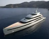 Un yacht de luxe gris clair navigue dans une baie. Le choix couleur coque bateau est élégant, contrastant avec le bleu profond de l'eau.