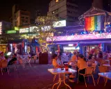 A vibrant night scene in gay Taipei, with people dining outdoors under colorful lights and a rainbow flag.