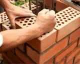Manos colocan ladrillo con huecos, mostrando sus dimensiones. Construcción de pared con mortero.
