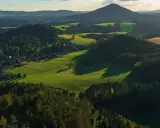 Malownicze góry w Czechach, zielone pola z balotami siana, lasy i niewielka wioska w dolinie.