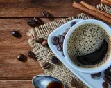 Heißer Kaffee mit Zimt, frisch zubereitet von einem Vollautomaten, duftet auf rustikalem Holz.